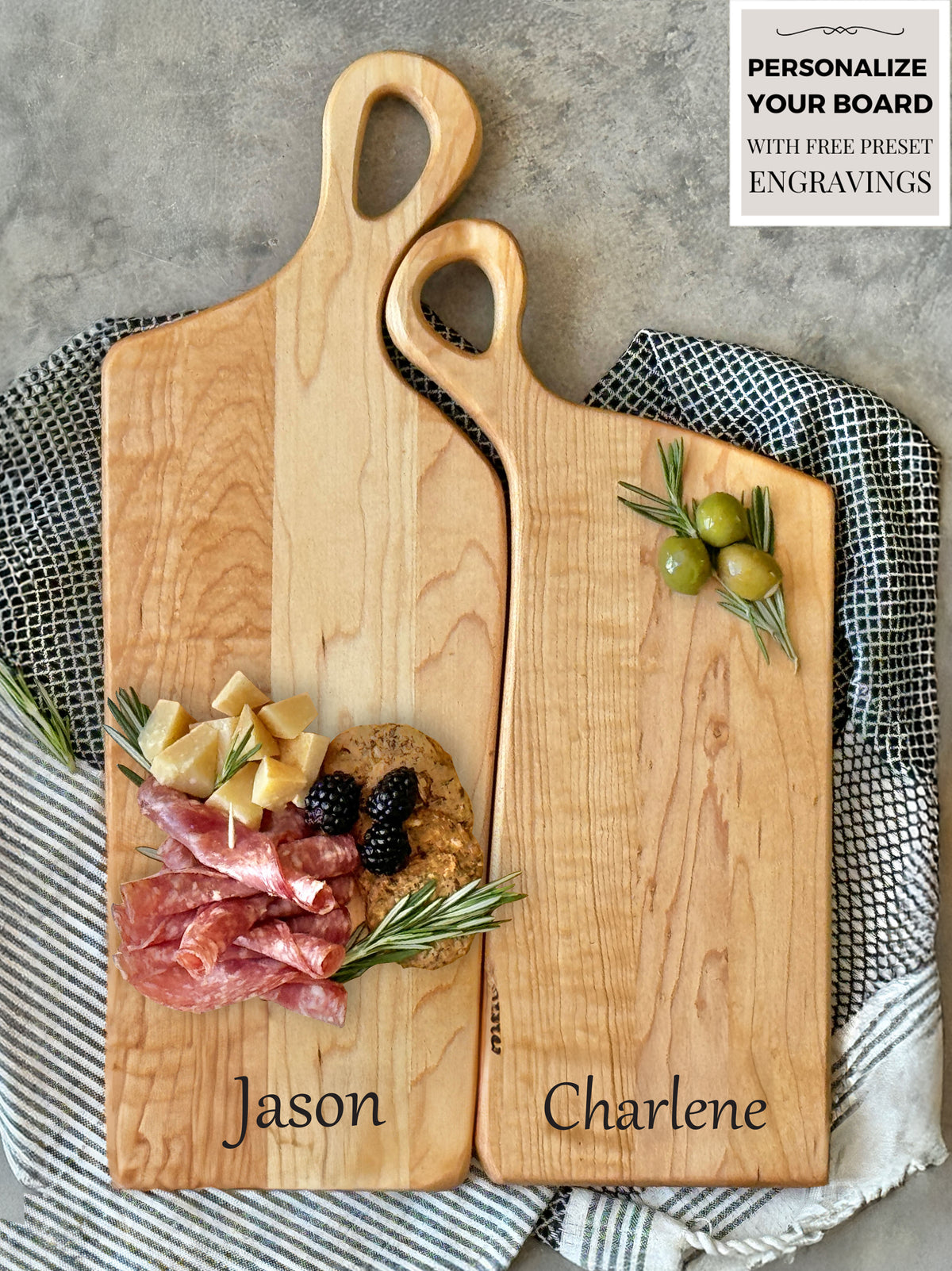 Two handcrafted wooden boards made from edge grain maple. Both feature ergonomic handles with a soft, rounded design, displayed on a textured fabric backdrop for a rustic aesthetic.