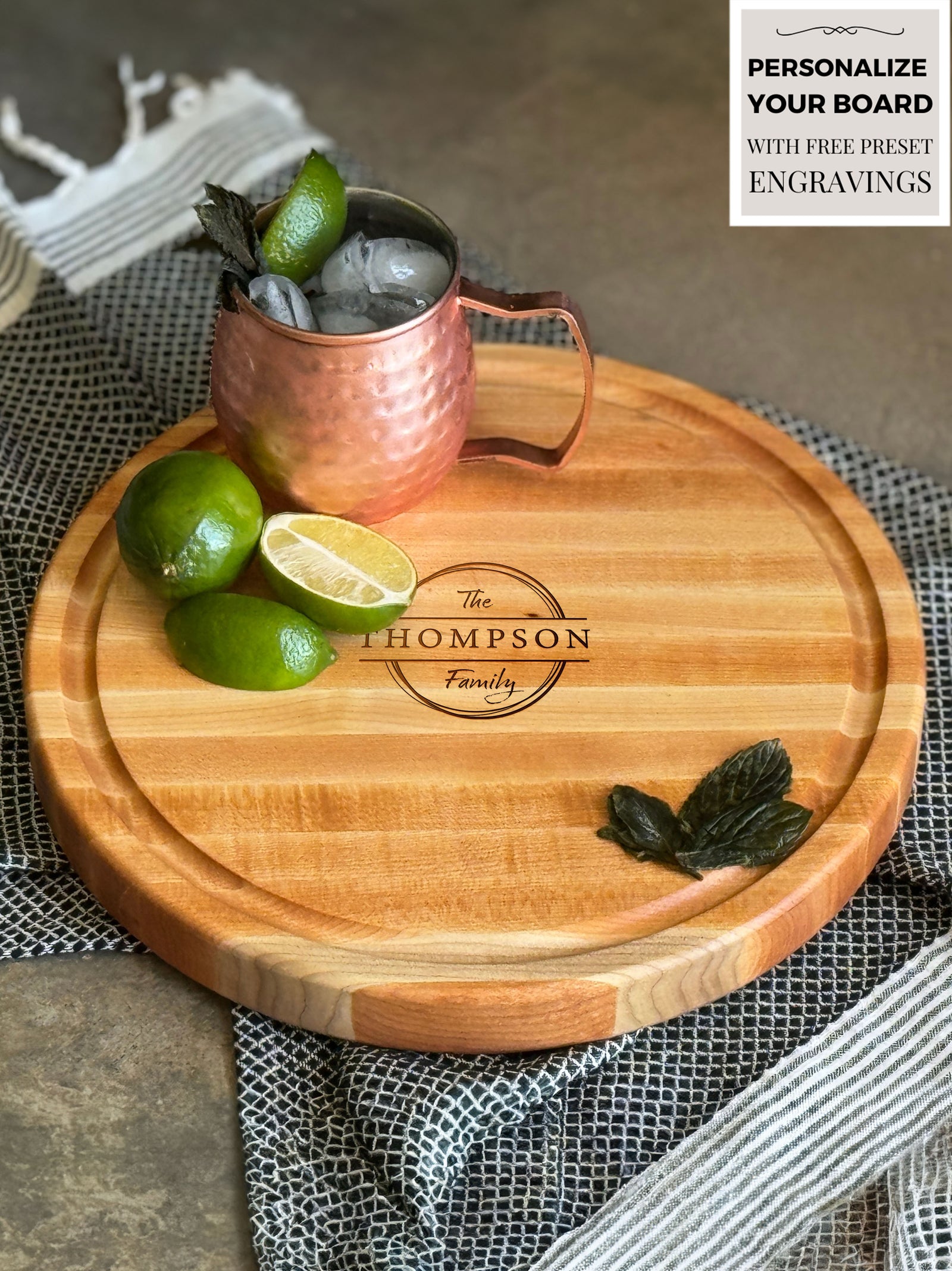 A round, personalized maple wood cutting or charcuterie board engraved with Forever Starts Here - Jordon & Ali - 07.20.24. The board has a juice groove and is topped with olives, feta, cherry tomatoes, salami, a cheese rose, almonds, blackberries, and fresh herbs.