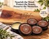 Four small black metal tins of Charcuterie board conditioning wax are arranged on a wooden surface in front of a large engraved wooden sign reading 'Andrew & Elyshia' and the date 'September 14th, 2025.' A cream circular badge says 'Sold in Packs of 4.