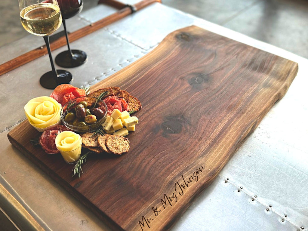 Black Walnut Live Edge Rustic No handle 26x 13 Cheese Board and cutting board with a beautiful arrangement of meats, cheeses, fruits and other foods with a large personalized engraving.