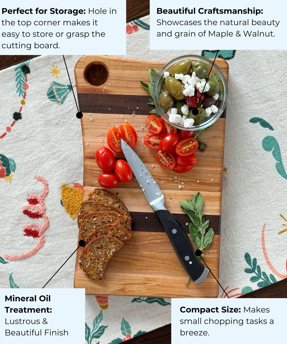 Compact maple and walnut cutting board with a corner hole for easy storage, shown with a knife, cherry tomatoes, crackers, and a bowl of olives with feta. Features include mineral oil treatment, beautiful craftsmanship, and a smooth, durable finish