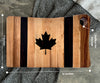 The striped maple and walnut canadian flag cutting board with a laser-engraved, epoxy filled maple leaf in the center. The board dimensions are illustrated 12 by 7 inches. a perfectly placed hole at the top meant for hanging.