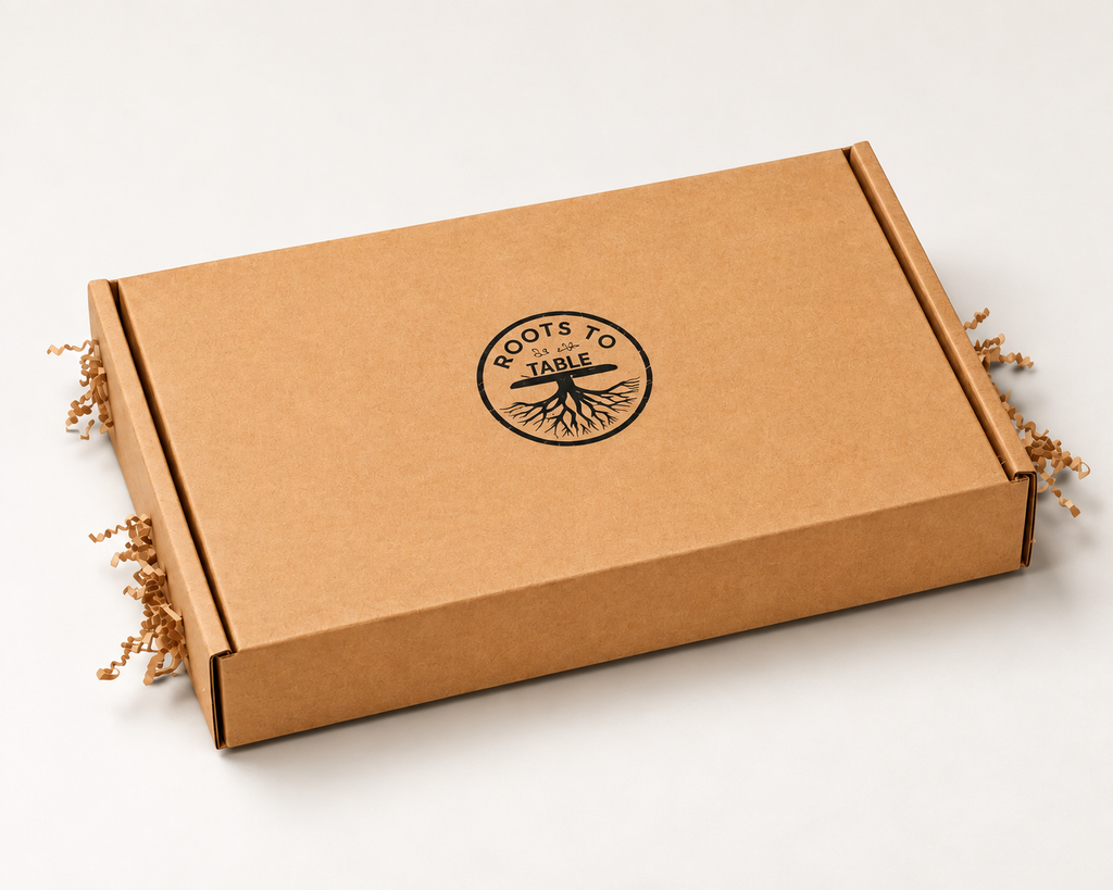 A square brown kraft cardboard box with a black printed circular logo reading 'ROOTS TO TABLE' in the center, photographed on a clean white background with crinkle paper filler visible at the sides. This is a gift ready personalized charcuterie board