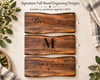 Three rustic engraved wooden sign designs displayed on a light neutral background with decorative greenery and a plaid cloth. Signature personalized engraving options on live edge charcuterie boards.