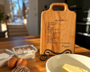Handwritten Chocolate Brownie recipe engraved onto a maple wood cutting board, sits on the kitchen counter with the ingredients ready for baking.