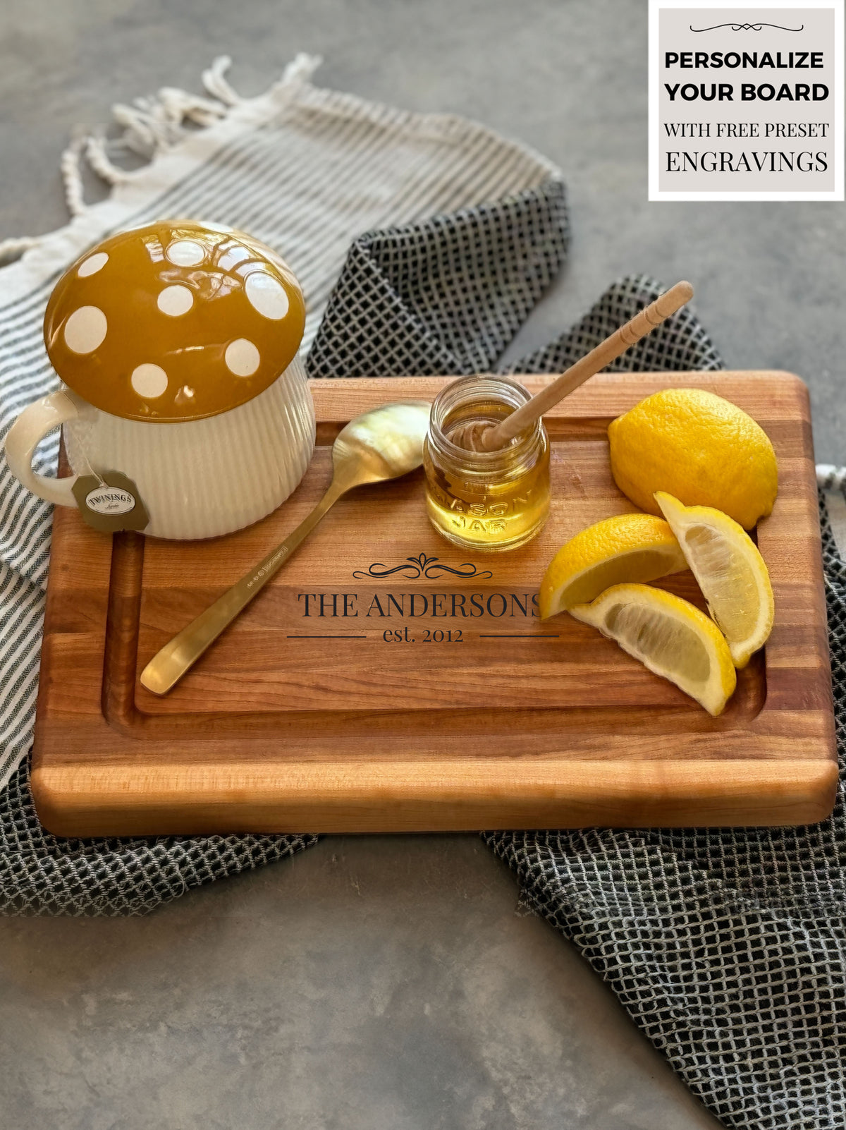 A small handcrafted wooden cutting board with a sleek juice groove, made from rich Canadian maple, resting on a patterned cloth, it showcases elegance and functionality.  The board is personalized and is being used to serve hot tea with honey and lemon wedges.