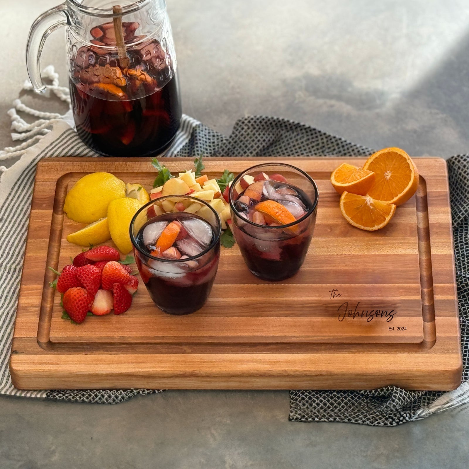 A handcrafted wooden cutting board with a sleek juice groove, made from rich Canadian maple, lies on a textured gray surface. Surrounded by vibrant red tomatoes, a paring knife, and patterned cloth, it showcases elegance and functionality.