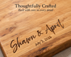 Close-up of a personalized wooden cutting board with engraved script text reading 'Shawn & April' and the date 'July 3, 2025,' plus overlaid marketing text at the top: 'Thoughtfully Crafted Built with care in every detail.'.