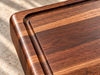 Close-up of a handcrafted walnut cutting board highlighting its rich natural wood grain, smooth rounded corners, precision-routed juice groove and carefully finished edges. Detailed view showcasing the craftsmanship and quality of a solid hardwood cutting board designed for food preparation, serving and personalized gift giving.