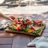 Live edge wooden charcuterie board with fresh fruit including watermelon, berries, and citrus served outdoors for entertaining