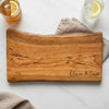 Wooden cutting board with 'Olivia & Liam' engraving on a white surface with drinks. Minimal cherry live edge charcuterie board with natural wood grain