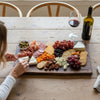 Person preparing to cut into cheese on a custom engraved charcuterie board gifted for a housewarming gathering