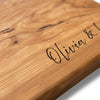 Wooden cutting board with engraved text on a light wood background. Close-up of engraved cherry live edge charcuterie board with custom name