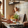 Woman preparing food in a kitchen with a cutting board and ingredients. A personalized charcuterie board leans against the wall as part of the kitchen decor