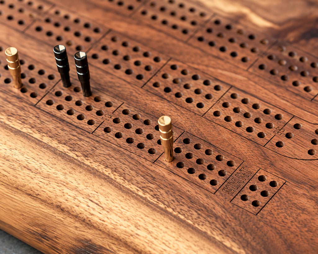 Close-up of an heirloom quality wooden cribbage board with engraved slots, round metal pegs.