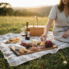 Person at a picnic in a field with a basket, wine, and custom live edge charcuterie board.