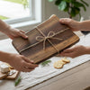 Two hands exchanging a wooden cutting board gift with personalized engraving 