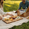 Couple having a picnic in a park with a natural live edge wooden serving board of food and wine glasses.