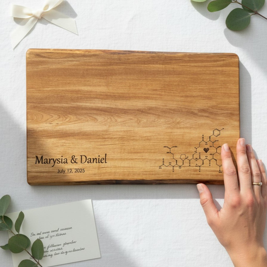 Wood cutting board with custom engraved names and date for a personalized wedding gift, placed on a white surface with a hand and card.