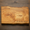 Wooden cutting board with 'Mr. & Mrs. Johnson' engraving on a wooden surface. Rustic cherry live edge charcuterie board with natural knots and grain.