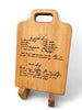 two hand written recipes engraved on a face grain maple cutting board, the board sits on a two piece stand.